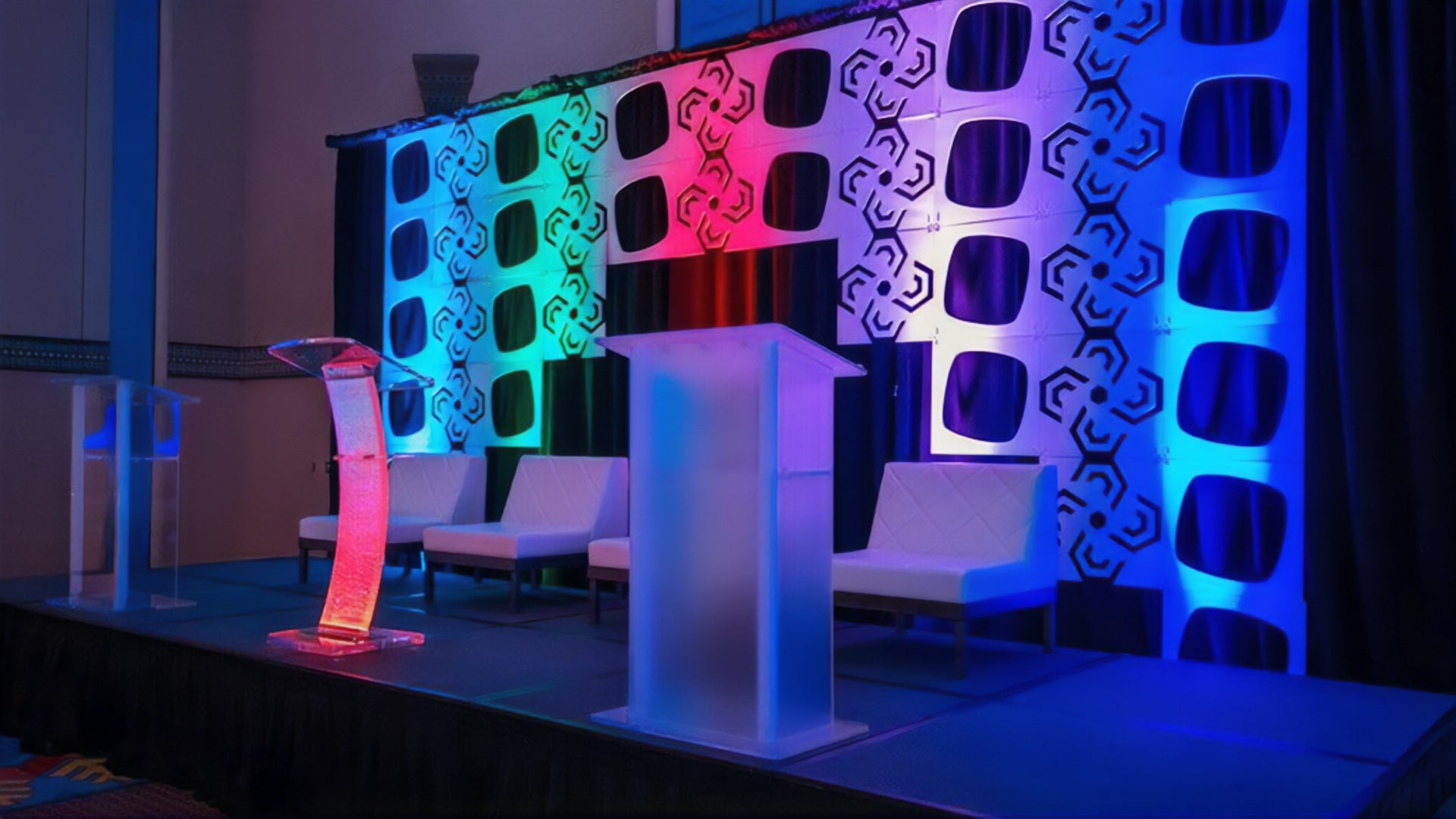 Lecterns on a stage with blue, green, and magenta patterned backdrop